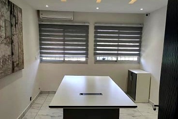 La même pièce devenue salle de réunion : table centrale, stores, éclairage intégré au plafond.